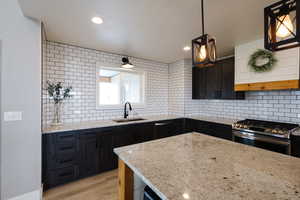 Kitchen with dark cabinets, backsplash, stainless steel appliances, and light stone counters