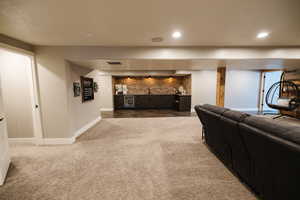 Carpeted living room featuring wet bar, beverage cooler, brick wall, and a textured ceiling