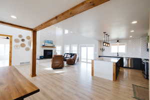 Kitchen featuring beamed ceiling, open floor plan, a kitchen island, light wood-type flooring, and a fireplace