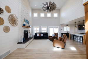 Living room featuring wooden walls, light wood-type flooring, a stone fireplace, recessed lighting, and a high ceiling