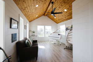 Living area with light wood finished floors, a ceiling fan, wood walls, recessed lighting, and a wood ceiling with exposed beams
