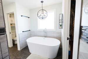 Bathroom featuring tile walls, a freestanding bath, a wainscoted wall, suspended lighting, and dark tile patterned flooring