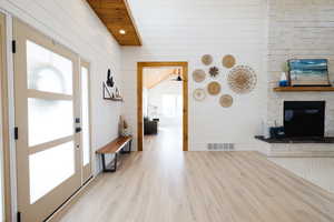 Entryway featuring light wood finished floors, wood walls, recessed lighting, wooden ceiling, and a large fireplace