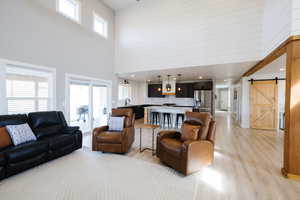 Living area with a barn door, light wood-style flooring, a high ceiling, wooden walls, and recessed lighting