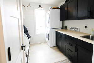 Laundry area featuring stacked washer and clothes dryer, cabinet space, and light wood-type flooring