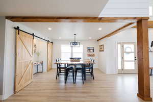 Dining room featuring a barn door, light wood-style flooring, wooden walls, and hanging lights