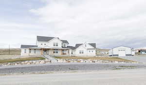 Modern farmhouse style home featuring covered porch, a detached garage, a shingled roof, and an outbuilding