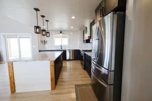 Kitchen with stainless steel appliances, a kitchen island, light wood-style flooring, decorative backsplash, and light stone countertops