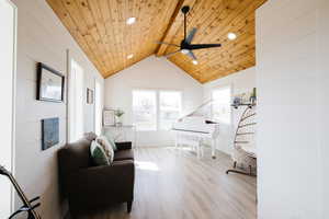 Living area with light wood finished floors, a ceiling fan, wood walls, a wooden ceiling with exposed beams, and recessed lighting