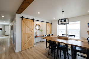 Dining area with a barn door, light wood finished floors, wooden walls, and hanging lights