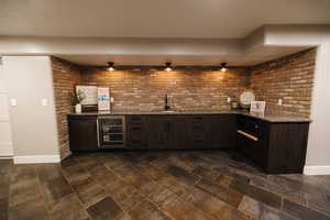 Indoor wet bar with dark wood finish cabinets, dark stone counters, beverage cooler, and a textured ceiling