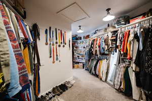 Walk in closet featuring attic access and light colored carpet