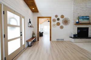 Entrance foyer with light wood finished floors, wood walls, recessed lighting, wooden ceiling, and a stone fireplace
