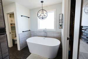 Bathroom with a freestanding bath, tile walls, a wainscoted wall, suspended lighting, and dark tile patterned floors