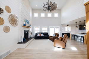 Living room with light wood finished floors, a stone fireplace, wood walls, recessed lighting, and a high ceiling