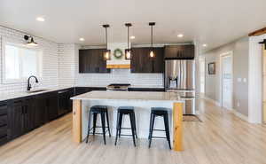 Kitchen featuring light stone countertops, stainless steel appliances, tasteful backsplash, light wood-style floors, and a center island