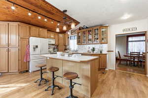Kitchen with a kitchen island, light countertops, white appliances, light wood-type flooring, and glass fronted cabinets