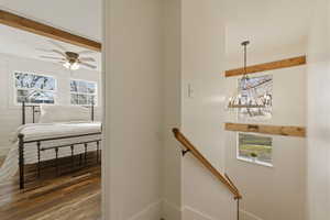 Stairway with wood finished floors, beam ceiling, a chandelier, and a ceiling fan