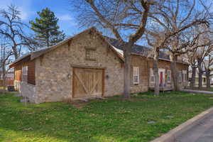 View of side of home with a yard, stone siding, and an outbuilding