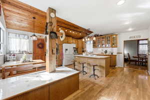 Kitchen featuring tile countertops, vaulted ceiling, light wood-type flooring, glass insert cabinets, and white fridge with ice dispenser