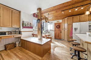 Kitchen with light countertops, light wood finished floors, wainscoting, white appliances, and a breakfast bar