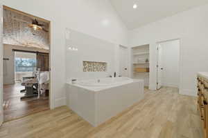 Ensuite bathroom with lofted ceiling, vanity, light wood-type flooring, a garden tub, and a walk in closet