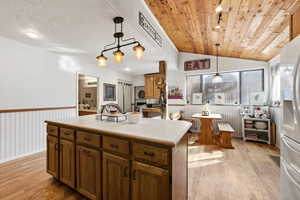 Kitchen featuring light countertops, wainscoting, stainless steel refrigerator with ice dispenser, vaulted ceiling, and light wood finished floors