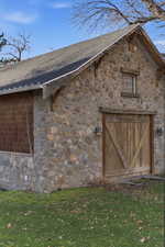View of home's exterior with stone siding, a yard, and roof with shingles