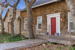View of exterior entry featuring a shingled roof and a wooden deck