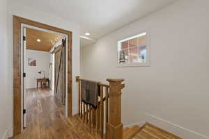 Hall with an upstairs landing, wood finished floors, a barn door, and recessed lighting