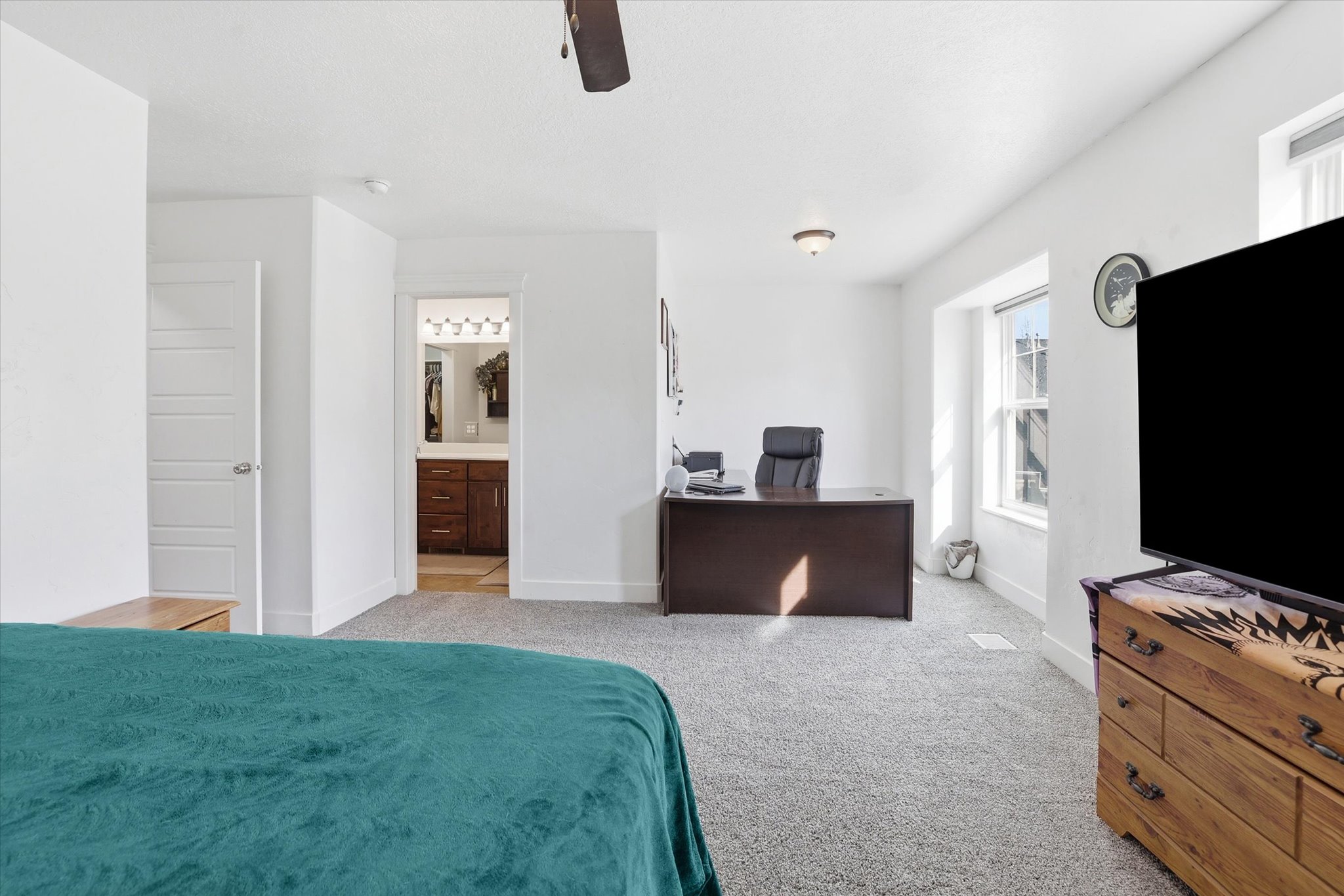 Bedroom with a desk, light carpet, ceiling fan, and connected bathroom