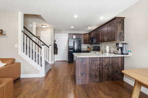 Kitchen featuring dark wood finish cabinets, black appliances, a peninsula, dark wood finished floors, and light stone countertops