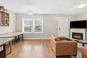 Living area featuring a glass covered fireplace, light wood finished floors, and a textured ceiling