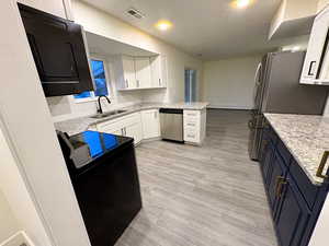 Kitchen featuring light stone countertops, black appliances, decorative backsplash, light wood-style flooring, and dual tone cabinetry