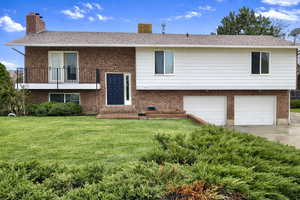Raised ranch featuring a chimney, a front yard, brick siding, and an attached garage