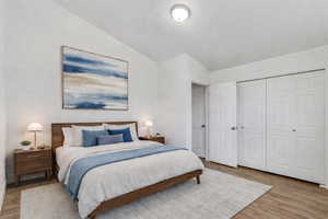 Bedroom with vaulted ceiling, wood finished floors, and a closet