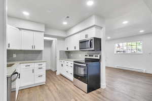 Kitchen featuring stainless steel appliances, white cabinetry, light stone counters, light wood-type flooring, and baseboard heating