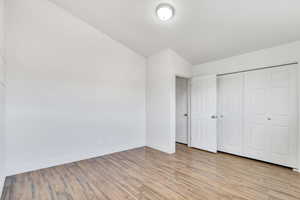 Unfurnished bedroom with light wood-style floors, a closet, and lofted ceiling