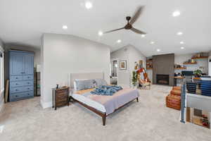 Bedroom with lofted ceiling, recessed lighting, a fireplace, ceiling fan, and light colored carpet