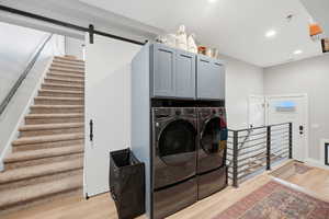 Laundry room featuring recessed lighting, a barn door, cabinet space, light wood finished floors, and separate washer and dryer