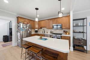 Kitchen with a breakfast bar, stainless steel appliances, ornamental molding, wood finish cabinets, and pendant lighting