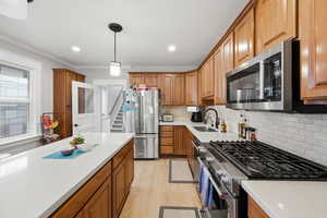Kitchen with stainless steel appliances, wood finish cabinets, light wood-style flooring, light stone counters, and crown molding