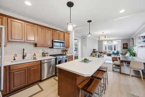 Kitchen with open floor plan, stainless steel appliances, wood finish cabinets, light countertops, and crown molding