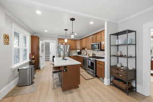 Kitchen with wood finish cabinetry, stainless steel appliances, light countertops, decorative light fixtures, and crown molding