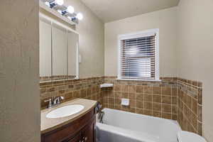 Bathroom featuring a textured wall, vanity, a textured ceiling, and a garden tub