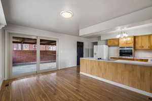 Kitchen featuring light countertops, oven, a peninsula, dark wood finished floors, and white fridge with ice dispenser