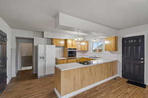 Kitchen featuring light countertops, white fridge with ice dispenser, a peninsula, dark wood-style flooring, and stainless steel oven