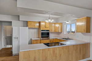 Kitchen featuring a peninsula, white refrigerator with ice dispenser, light countertops, and oven
