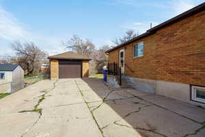View of side of home featuring an outbuilding, brick siding, concrete driveway, and a garage