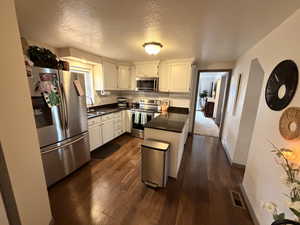 Kitchen featuring stainless steel appliances, white cabinets, tasteful backsplash, dark wood-type flooring, and a textured ceiling